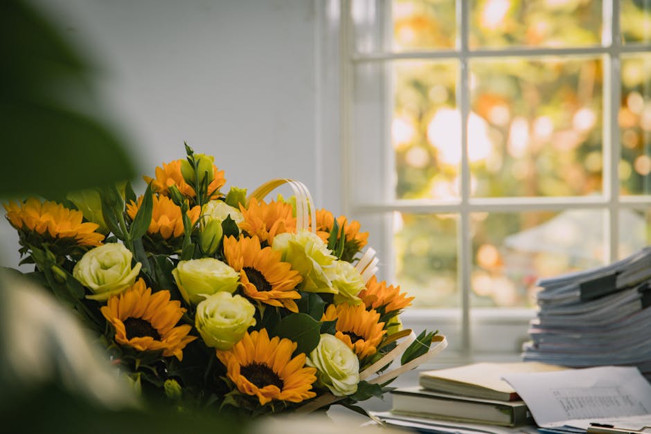 A vibrant floral arrangement in a cream-colored ceramic vase featuring deep pink, fuchsia, and red carnations complemented by soft gray-green eucalyptus leaves, arranged on a white table against a pla